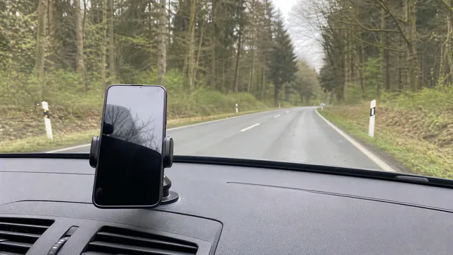 A phone mounted on a car dashboard overlooking a winding German road through forested hills